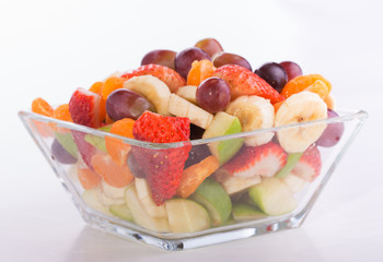 Fruit salad in rich colors in a glass bowl, on light background
