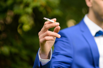 Gentleman smokes a cigarette. Imposing man in a blue suit exquisitely smokes. Imposing the male is dressed.