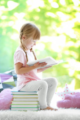 Beautiful little girl sitting on pile of books near window