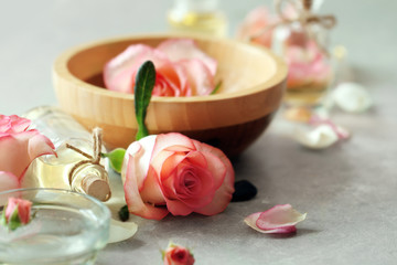 Fototapeta na wymiar Bottle of aroma oil with roses in wooden bowl on table