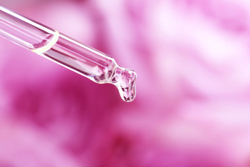 Pipette with essential oil on blurred flowers background, closeup
