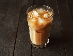 Glass of coffee with cream and ice on wooden table