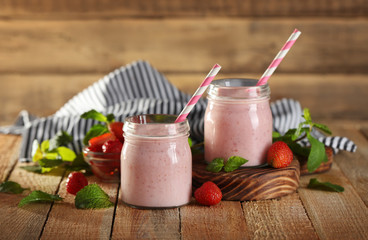 Glass jars with delicious strawberry milkshake, napkin and berries on wooden table