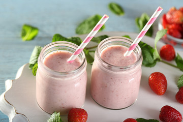 Glass jars with delicious strawberry milkshake and berries on blue table