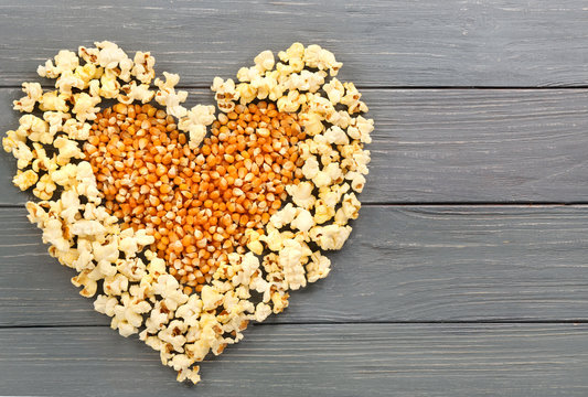 Heart made of popcorn and maize grains on wooden background, top view