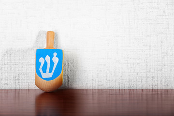 Dreidel for Hanukkah on wooden table against light textured wall