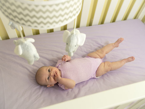 Infant Baby in Purple Crib with Elephant Mobile Smiling at Camera
