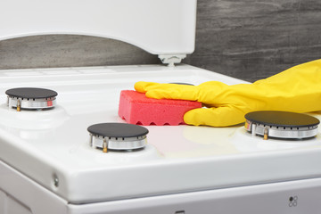 Hand in yellow glove cleaning white stove with pink sponge