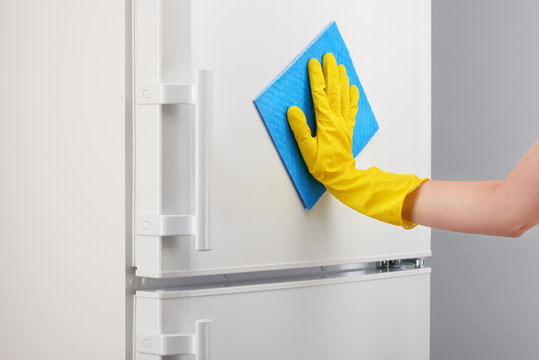 Hand in yellow glove cleaning white refrigerator with blue rag
