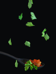 Black spoon with meat and tomato sauce and parsley leaves falling. Background: total black.