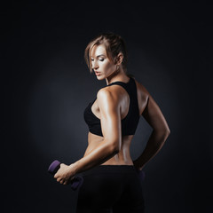 Fototapeta na wymiar Muscular fitness woman posing on a dark background in studio