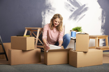 The start of a new chapter of life. Shot of a smiling middle aged woman sitting surrounded with a cardboard box while moving into a new home and painting the wall.