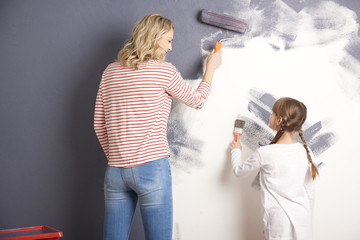 Decorating the wall together. Portrait of a mother and her cute daughter painting wall together in their new home.