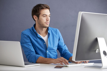 Thinking young man. Shot of a casual young businessman sitting at office in front of computer and working online. 
