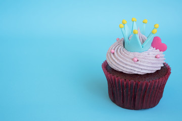 Cupcake with crown and pink heart over blue background