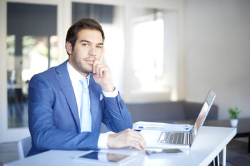Naklejka premium Shot of a young financial businessman with laptop sitting at desk in his office.