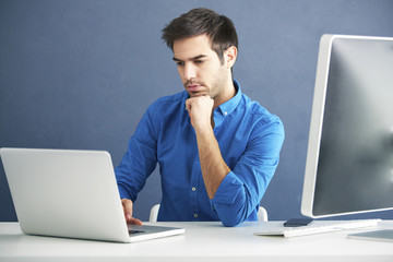 Thinking young man. Shot of a casual young businessman sitting at office in front of computer and working online. 