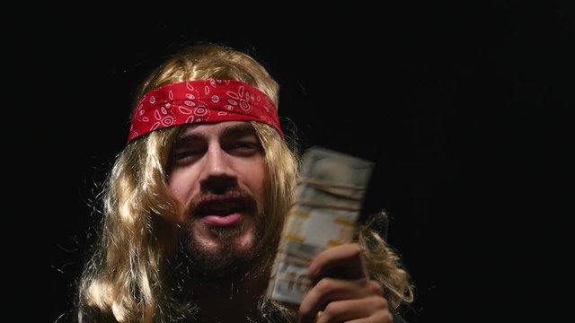 Funny looking rockstar showing a enormous pile of cash money to the camera and talking.