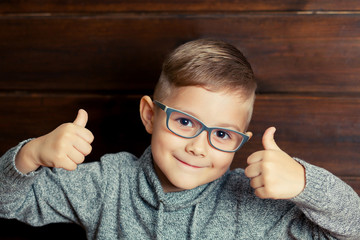 Child with glasses gives a thumbs-up.
