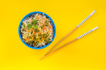 Bowl of instant noodles on yellow background. Chopsticks.