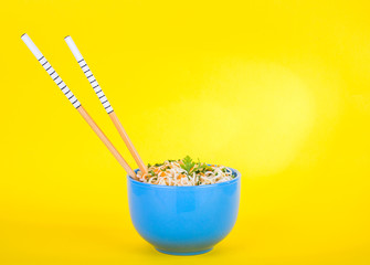 Bowl of instant noodles on yellow background. Chopsticks.