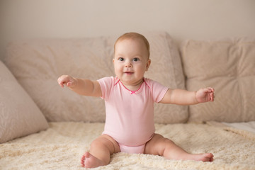 Cute smiling baby in pink bodysuit on a beige couch... - 127852177
