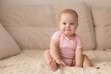 Cute smiling baby in pink bodysuit on a beige couch... - 127852185