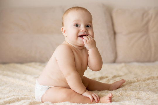 Cute smiling baby in diapers on a beige couch.