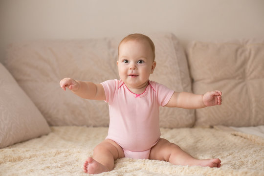 Cute smiling baby in pink bodysuit on a beige couch...