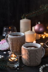 Obraz na płótnie Canvas Two cups in knitted mittens of fresh hot cocoa or chocolate on wooden christmas background, dark photo
