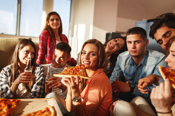 A lively group of friends gathers for a home party, eating delightful slices of pizza while sharing laughter and creating lasting memories.