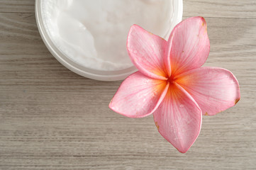 Body lotion in a container with a pink frangipani flower