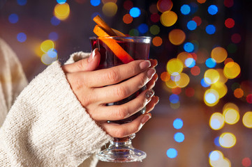 Glass with mulled wine in the hands of a girl on the background of Christmas lights