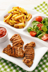 Grilled pork tenderloin, salad, and fried potatoes on white plate.