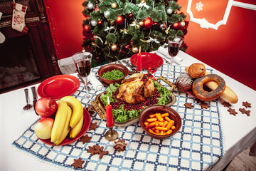 Christmas dinner by candlelight, table setting. Thanksgiving table with baked turkey in a decorated room with a Christmas tree.