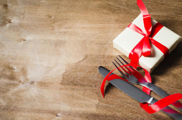 Fototapeta na wymiar Present and Cutlery Decorated with Red Ribbon on Wooden Background.