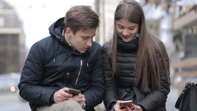 Young couple sitting on bench in the city and watching on smartphone