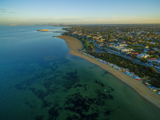 Aerial view of sunrise at Brighton Beach coastline with beach boxes, and CBD in the distance. Melbourne, Victoria, Australia.