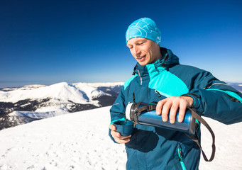 Happy young man drink hot tea during hiking on mountain in winter