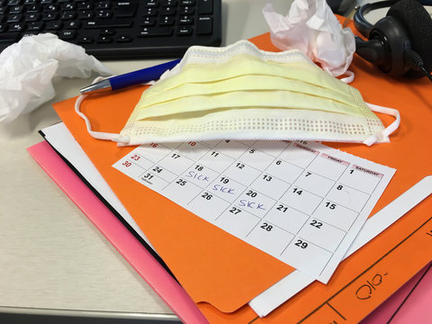 Desk in Office with tissues, files, medical face mask, and calendar showing sick days and absenteeism
