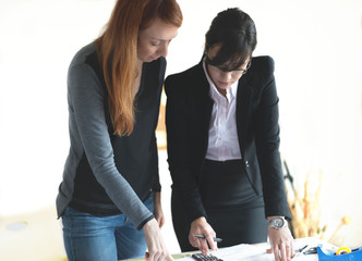Young redhead female architect and young female investor working in the office. Selective focus and small depth of field.