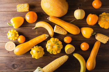Yellow fruits and vegetables on a    wooden background.  Colorful festive still life. Copyspace. Yellow squash, melon, lemon, banana, pepper, apples, corn