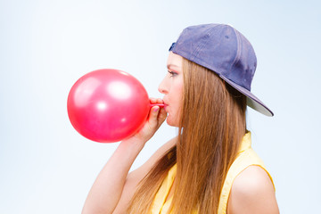 Female teenager inflating red balloon.