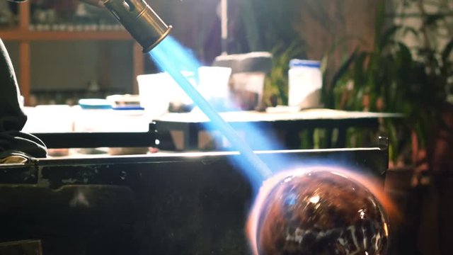 Glassblower blowing propane gas flame on finished piece of glass