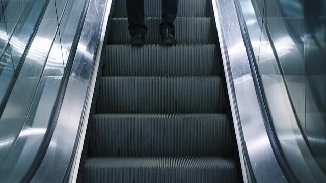 Close-up shot of young man with bag moving on escalator,  traveling on train. Rush hour, subway underground station. Modern escalator stairs moving up.