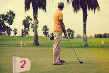Obraz premium Retro vintage image rear view of male golfer holding wooden golf club, green field outdoors background