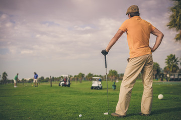 Obraz premium Rear view of male golfer holding metal golf club, green field outdoors background