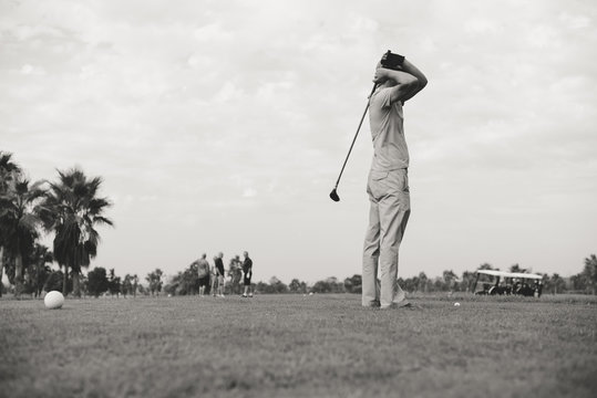 Retro vintage image rear view of male golfer holding wooden golf club, green field outdoors background