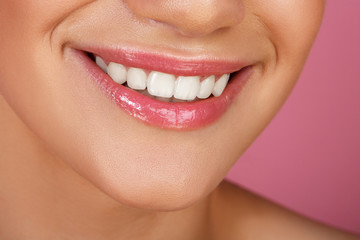 Beautiful smile with whitening teeth. Dental photo. Macro closeup of perfect female mouth, lipscare. Perfect pink lip makeup. Perfect clean skin, light fresh lip make-up. Pink background