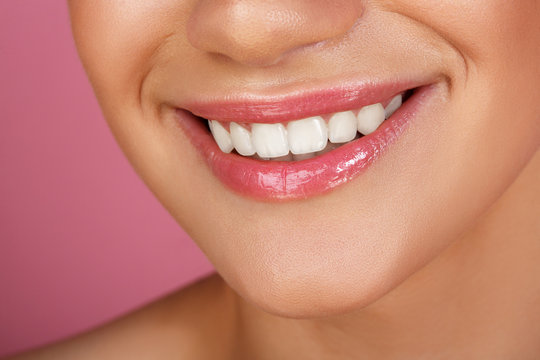 Beautiful smile with whitening teeth. Dental photo. Macro closeup of perfect female mouth, lipscare. Perfect pink lip makeup. Perfect clean skin, light fresh lip make-up. Pink background
